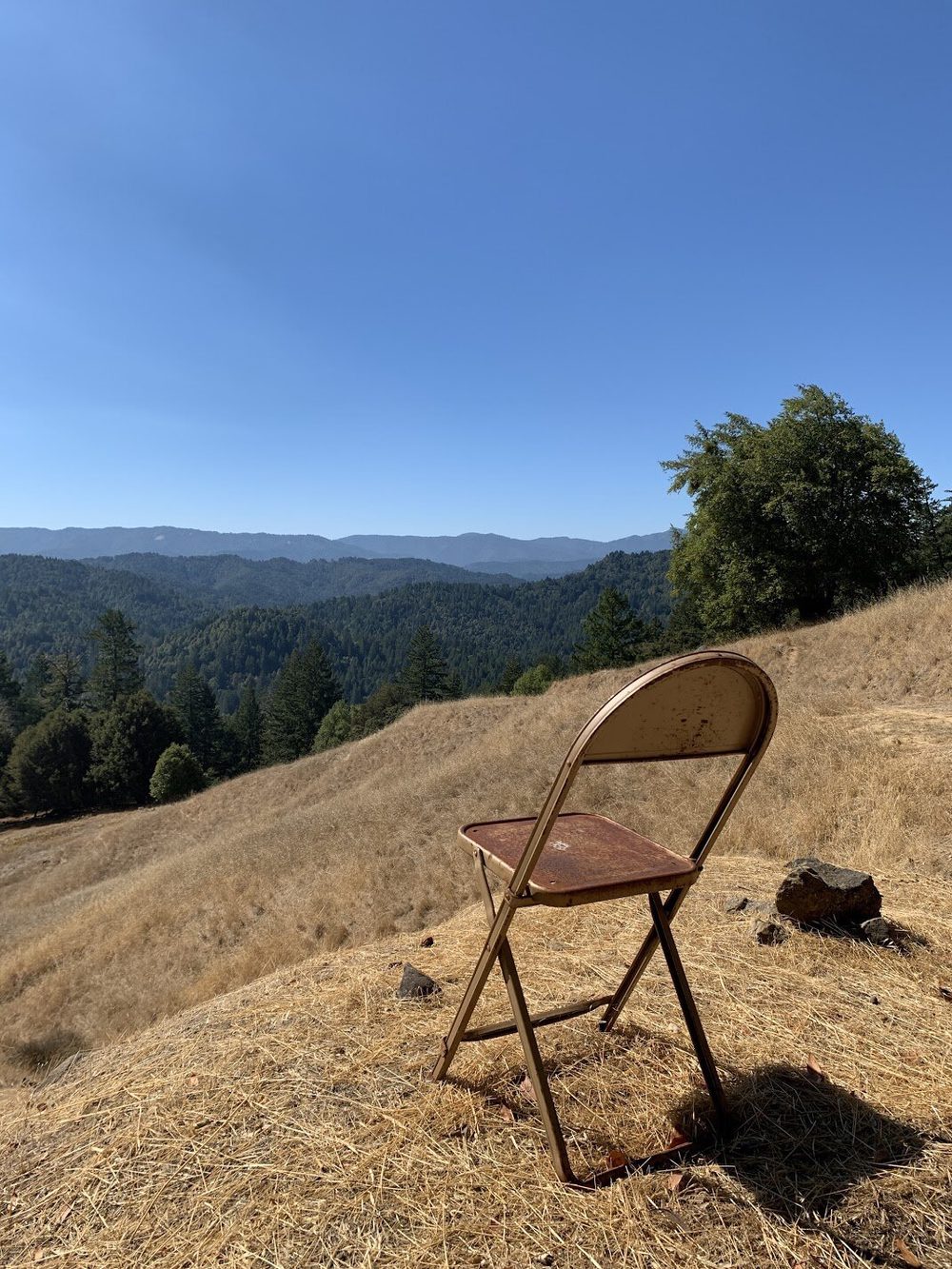 An old metal folding chair on a dry hilltop overlooking forested ridges.